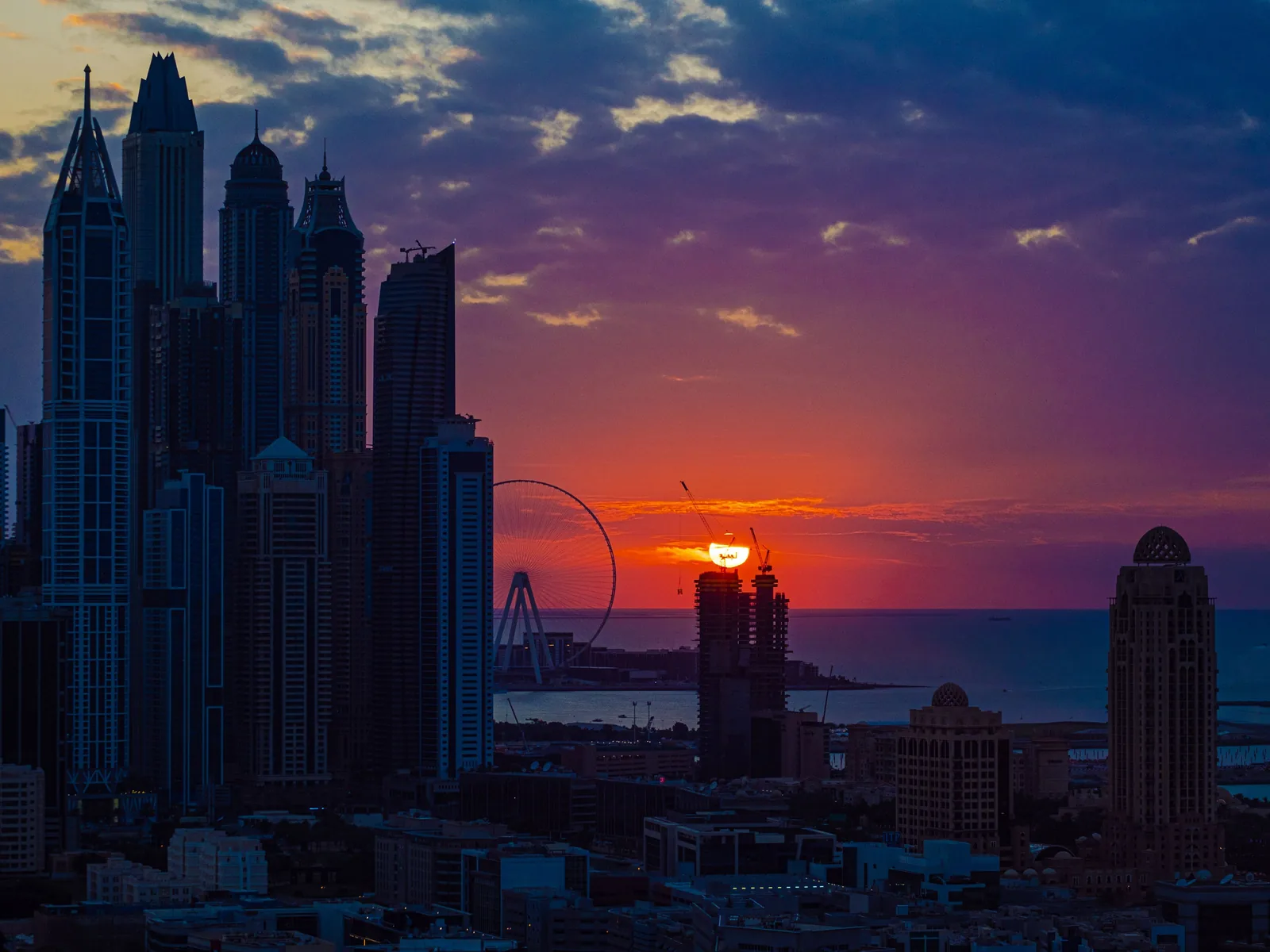 Breathtaking view of Dubai's skyline at sunset, featuring iconic skyscrapers and a serene Ferris wheel over the water