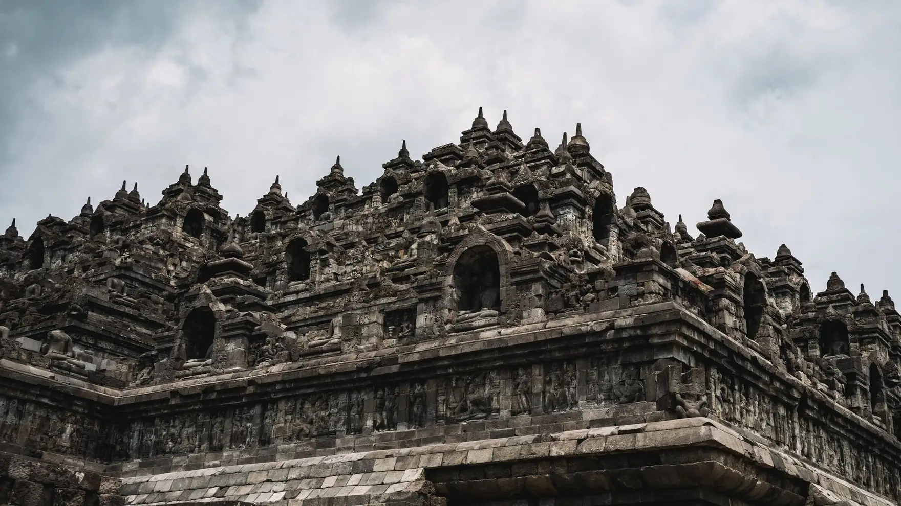 Majestic view of the ancient Borobudur Temple, showcasing intricate stone carvings under a cloudy sky