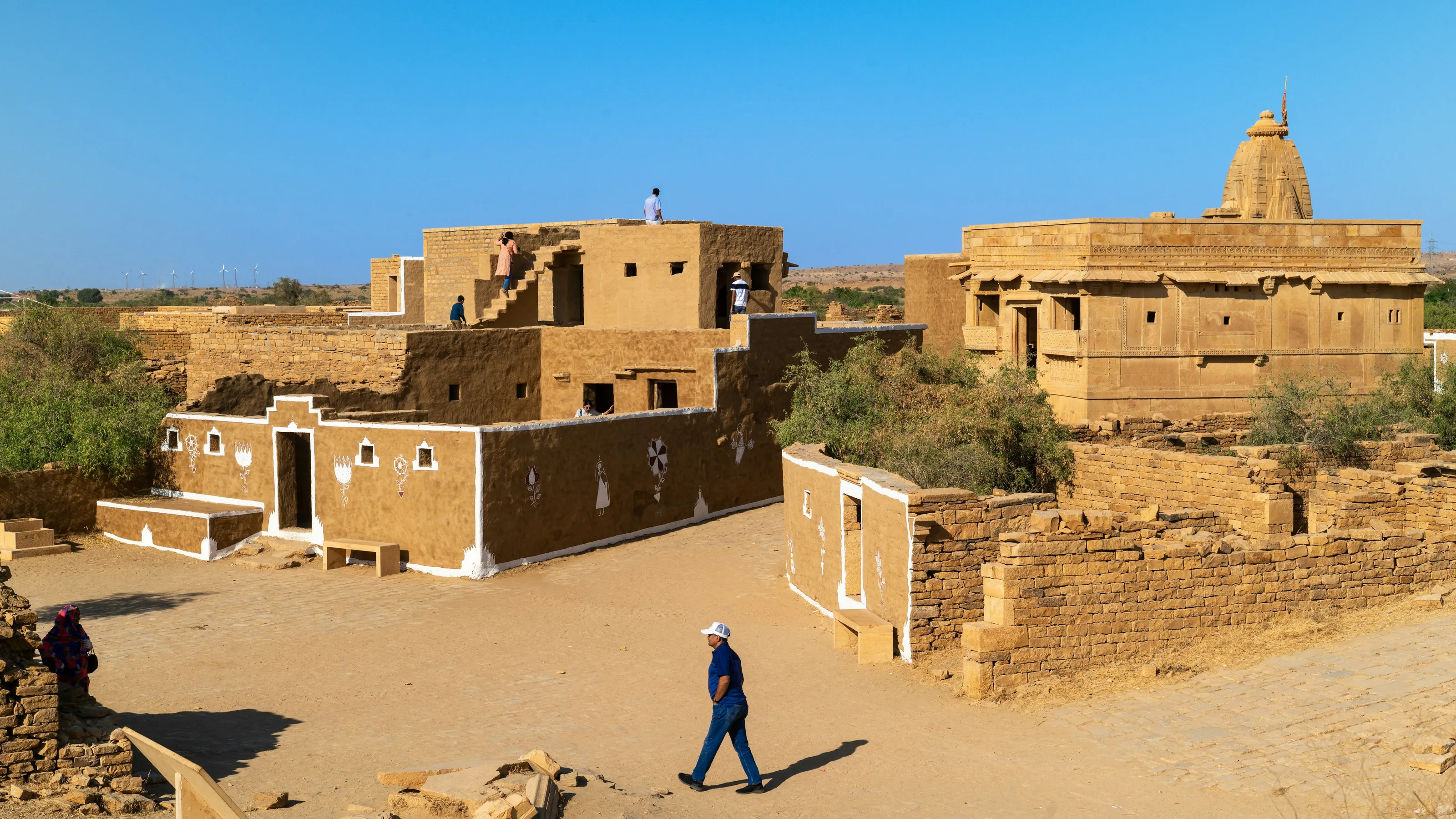 The abandoned sandstone houses of Kuldhara under a clear sky, the temple spire behind