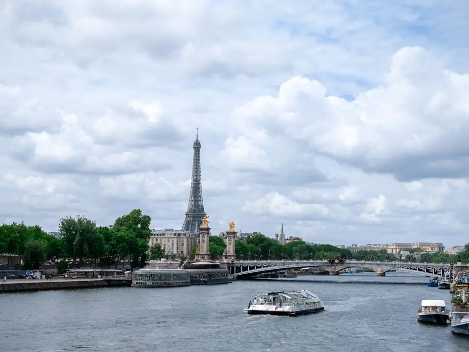 Scenic view of the Eiffel Tower and Seine River in Paris with a bridge and boats under a cloudy sky