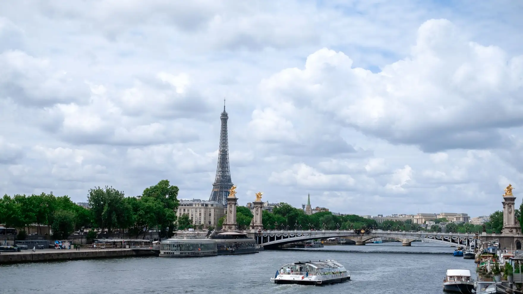 Scenic view of the Eiffel Tower and Seine River in Paris with a bridge and boats under a cloudy sky