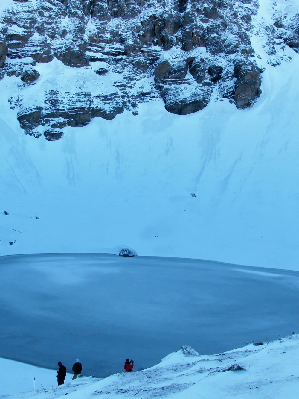 Roopkund lake frozen under snow, trekkers on its rim