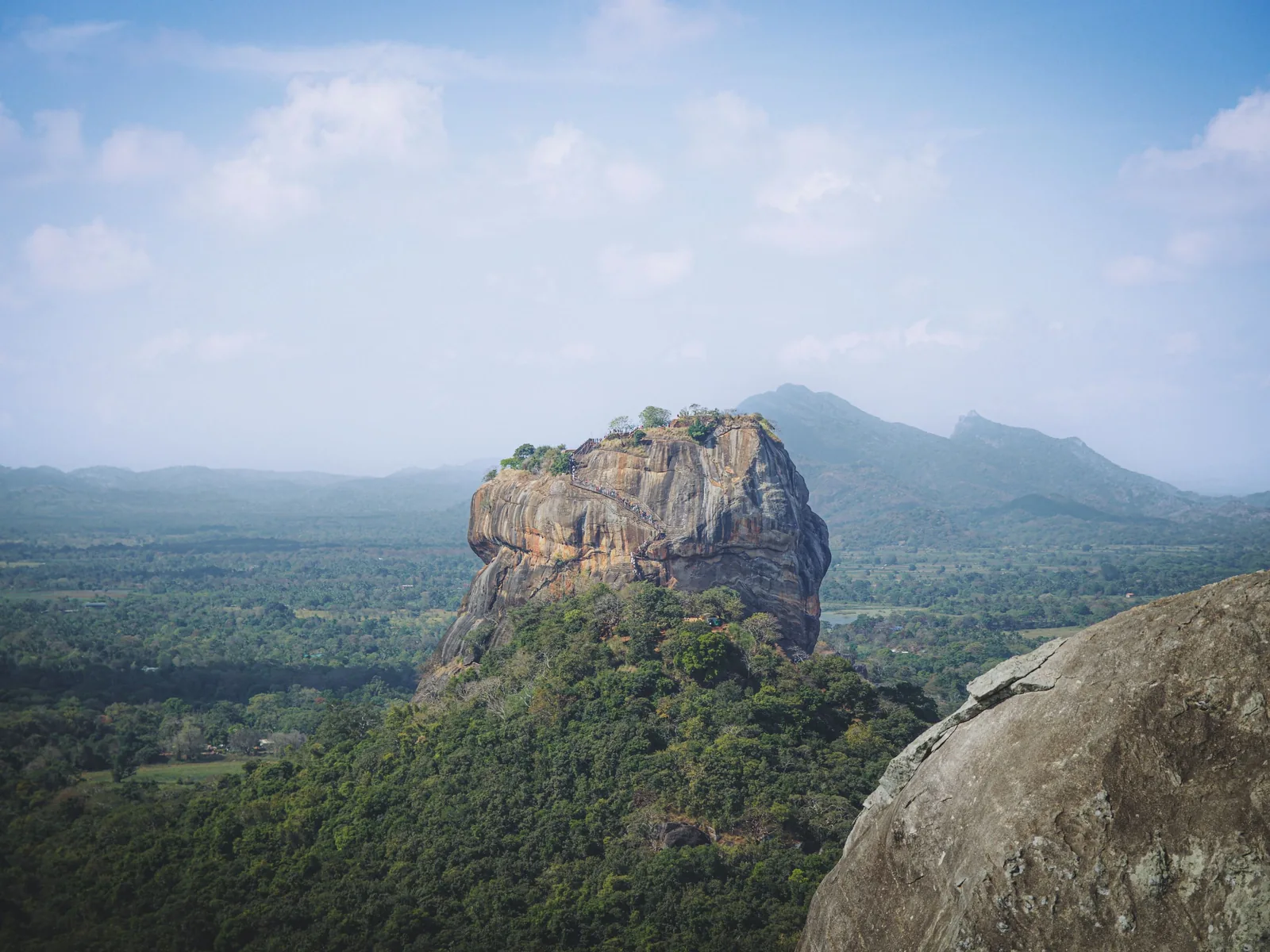 A stunning view of Sigiriya Rock Fortress in Sri Lanka, surrounded by lush greenery under a bright blue sky